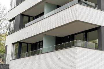 Moderní budova s bílou cihlovou fasádou a balkony s celoskleněným zábradlím.