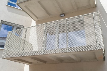 Balkón Modřanský Cukrovar s kovovým zábradlím na moderní budově proti modré obloze.