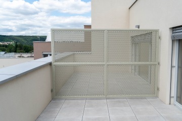 Balkon Modřanský Cukrovar AB s kovovým mřížkovým plotem, moderní dlažba, výhled na zelenou krajinu a oblačnou oblohu.