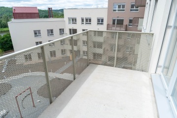 Balkón Modřanský Cukrovar s kovovým zábradlím a výhledem na moderní bytové budovy a zelenou krajinu.