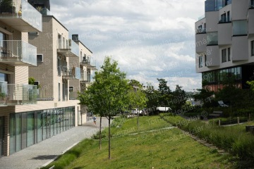 Moderní bytové domy s balkony, upravené trávníky a chodníky, oblačné nebe.