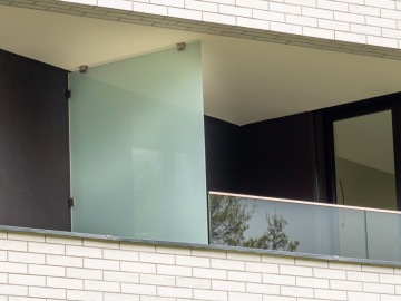 Balkon s dělící stěnou a skleněným zábradlím na moderní budově.