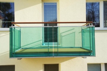 Zelené skleněné zábradlí balkonu na béžové omítce budovy Dolní Kounice.