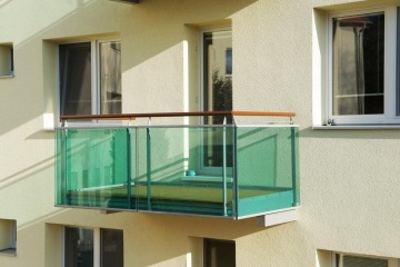 Skleněný balkon s matným zeleným zábradlím na žluté fasádě domu Dolní Kounice.