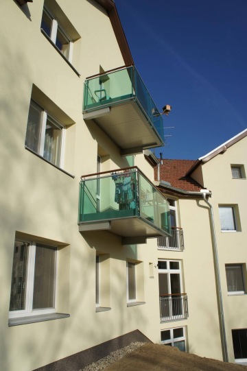 Balkony se skleněným zábradlím na světlém bytovém domě Dolní Kounice pod modrou oblohou.