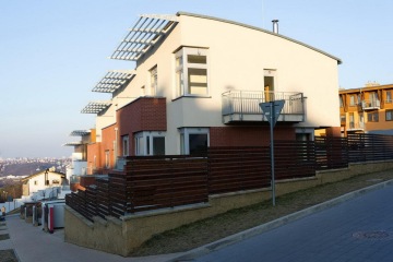 Moderní řadové domy s cihlovými fasádami na mírně svažité ulici za slunečného dne.