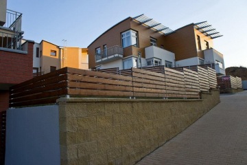 Moderní bytový dům s dřevěným oplocením a terasou ve svahu.