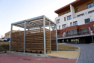 Dřevěný přístřešek na odpad poblíž moderního bytového domu.