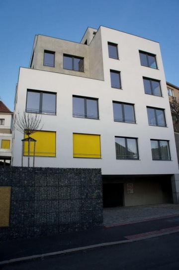 Moderní bytový dům Nad Vinohradem s bílou fasádou a žlutými okenními roletami na klidné ulici.
