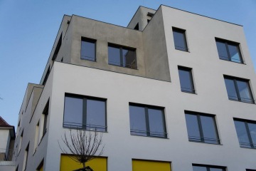 Moderní bytový dům Nad Vinohradem s geometrickými tvary a velkými okny proti modré obloze.