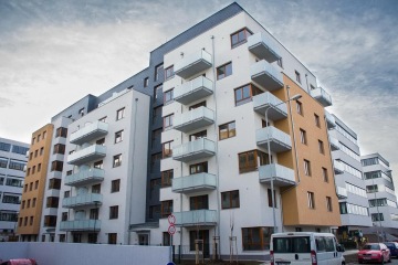 Moderní bytový dům s balkony a barevnou fasádou pod zamračenou oblohou.