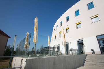 Moderní terasa Centrální depozitář UPM s kovovými židlemi a skleněným zábradlím pod modrou oblohou.