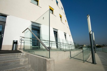 Moderní budova Centrální depozitář UPM s proskleným zábradlím a rampou, jasná obloha.