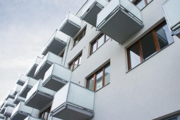 Moderní bytový dům s řadou prosklených balkonů a dřevěnými rámy oken.