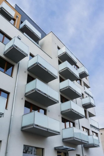 Moderní bytový dům s prosklenými balkony a modrou oblohou.