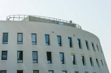 Moderní budova Centrální depozitář UPM s obloukovými okny a proskleným zábradlím na střeše.