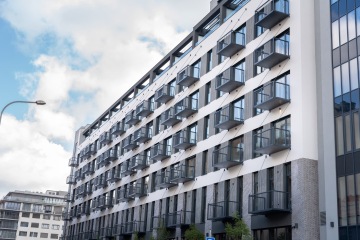 Moderní bytová budova s řadami skleněných balkonů pod modrou oblohou.