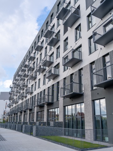 Moderní bytový dům s balkóny a cihlovou fasádou pod modrou oblohou.