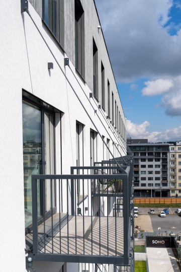 Moderní budova s balkony a panoramatickým pohledem na město pod částečně zataženou oblohou.