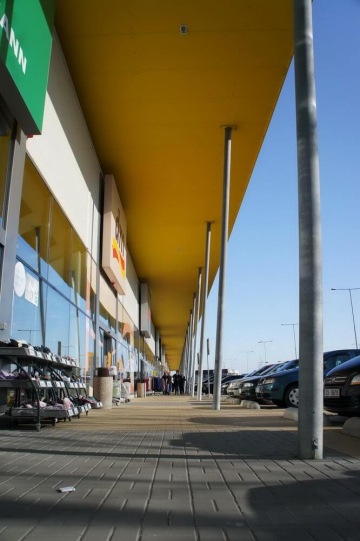 Obchodní centrum s řadou zaparkovaných aut a žlutou střechou podél prosklené stěny.