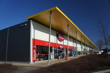 Nákupní centrum s obchodem Hervis, moderní architektura a žlutá střecha za slunečného dne.