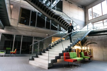 Moderní interiér budovy Jihočeské Univerzita se skleněnými schody a barevnými sedačkami, postava schází dolů.
