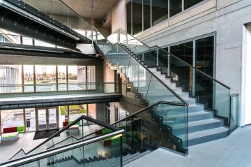 Moderní interiér Jihočeské Univerzity s proskleným zábradlím a průmyslovými prvky, schodiště v administrativní budově.
