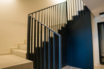 Moderní schodiště BD Krejcárek s kovovým zábradlím a tmavě modrou stěnou.