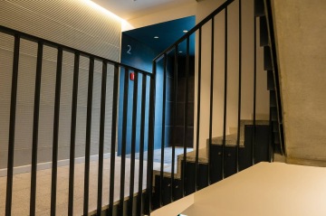 Schodiště s kovovým zábradlím vedoucí do moderního interiéru BD Krejcárek s modrou zdí a číslováním patra "2".