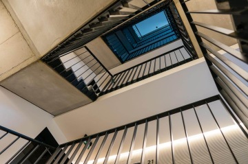 Schodiště BD Krejcárek s kovovým zábradlím pohledem nahoru vytváří geometrické tvary.