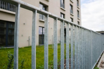 Kovový plot před moderním bytovým domem BD Krejcárek s trávníkem.