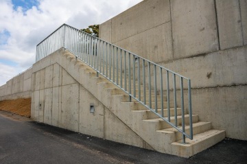 Betonové schodiště BD Krejcárek s kovovým zábradlím vedoucí na vyvýšený chodník pod zataženou oblohou.