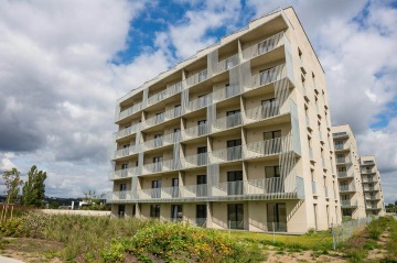 Moderní šestipodlažní bytový dům BD Krejcárek se zasazenou zelení a modrou oblohou.