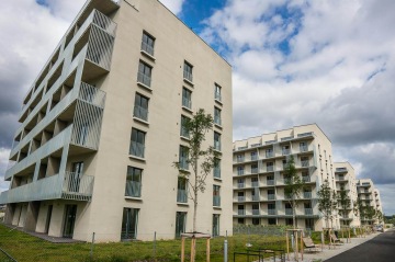 Moderní bytové domy BD Krejcárek pod zamračenou oblohou, s balkony a mladými stromy v popředí.