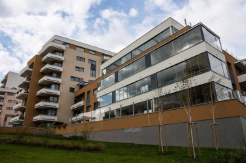 Moderní bytový dům BD Nad Modřanskou s prosklenými balkony a zasazený do zeleně pod modrou oblohou.