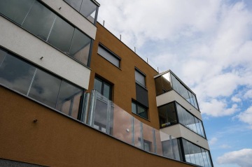 Moderní bytový dům BD Nad Modřanskou s velkými okny a proskleným zábradlím pod modrou oblohou.