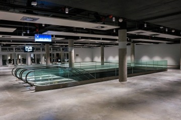 Prázdné obchodní centrum O2 Universum Praha s eskalátory, betonovou podlahou a svítícími reklamami.