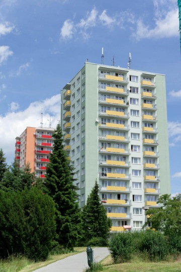 Vysoké panelové domy se závěsnými balkony a parky kolem, modrá obloha.