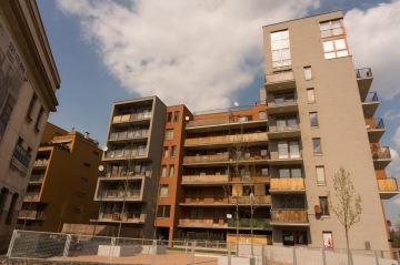 Moderní bytový dům s balkony a satelitními anténami pod modrou oblohou.