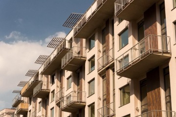 Moderní bytový dům X Loft s prosklenými balkóny a kovovými stínidly proti modré obloze.