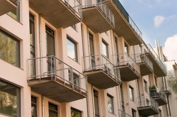 Moderní bytový dům X Loft s balkóny, velkými okny a světlou fasádou pod modrou oblohou.