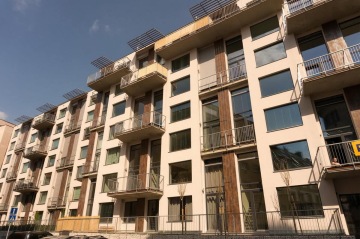 Moderní bytový dům X Loft s balkóny a velkými okny za slunečného dne.