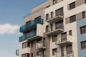Moderní bytový dům s balkony a modrými skleněnými zábradlími.