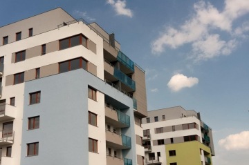 Moderní bytové domy s balkony na pozadí modré oblohy s obláčky.