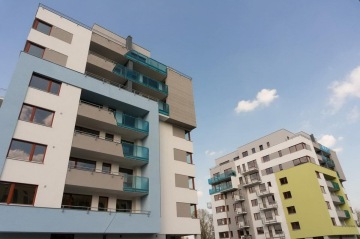 Moderní bytové domy s balkony a barevnými fasádami pod modrou oblohou.