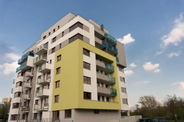 Moderní bytový dům s barevnými balkony na jasné obloze.