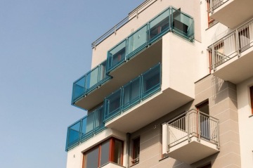 Moderní bytový dům s modrými skleněnými balkony na fasádě.