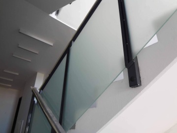 Skleněné zábradlí s kovovým rámem na vnitřním schodišti.