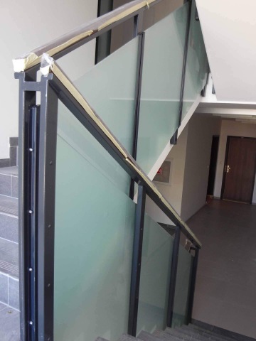 Skleněné zábradlí na vnitřním schodišti s kovovým rámem.