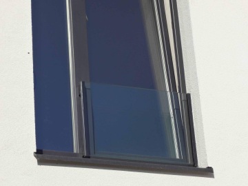 Skleněné zábradlí na okně moderní budovy s bílou fasádou.